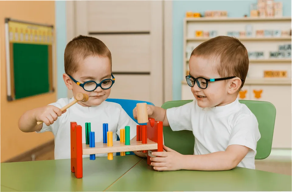 Two children playing with a wooden hammer toy at a table